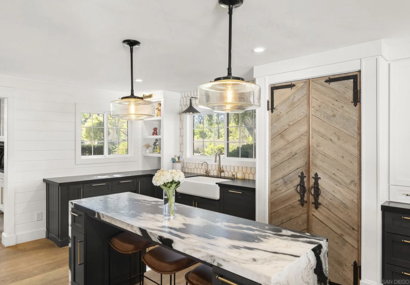 Modern kitchen featuring a marble island, black cabinetry, large window, and rustic wood sliding doors, showcasing open and airy design.