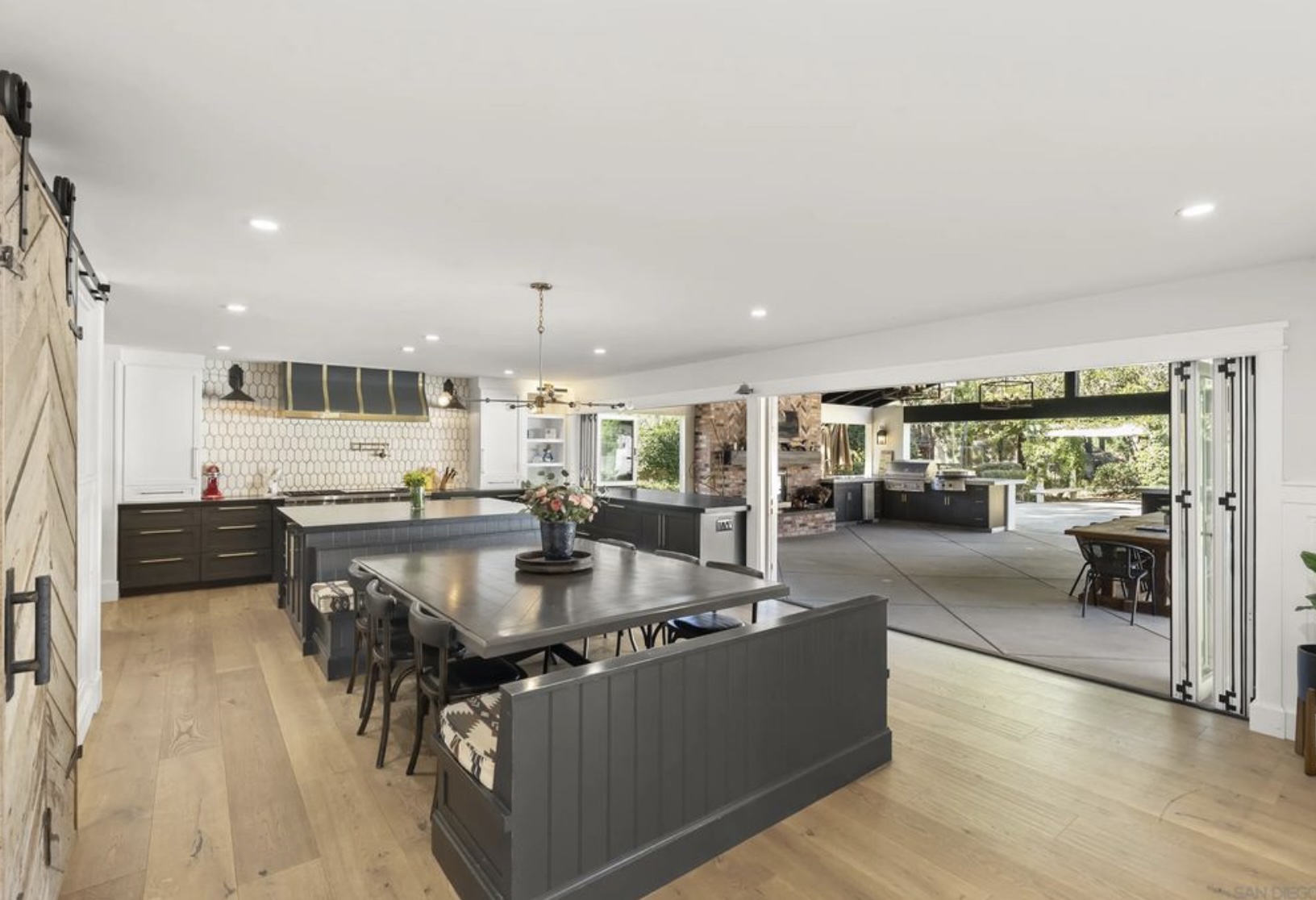 Spacious kitchen with dark cabinetry and a large dining area, featuring an open doorway leading to an outdoor barbecuing space.