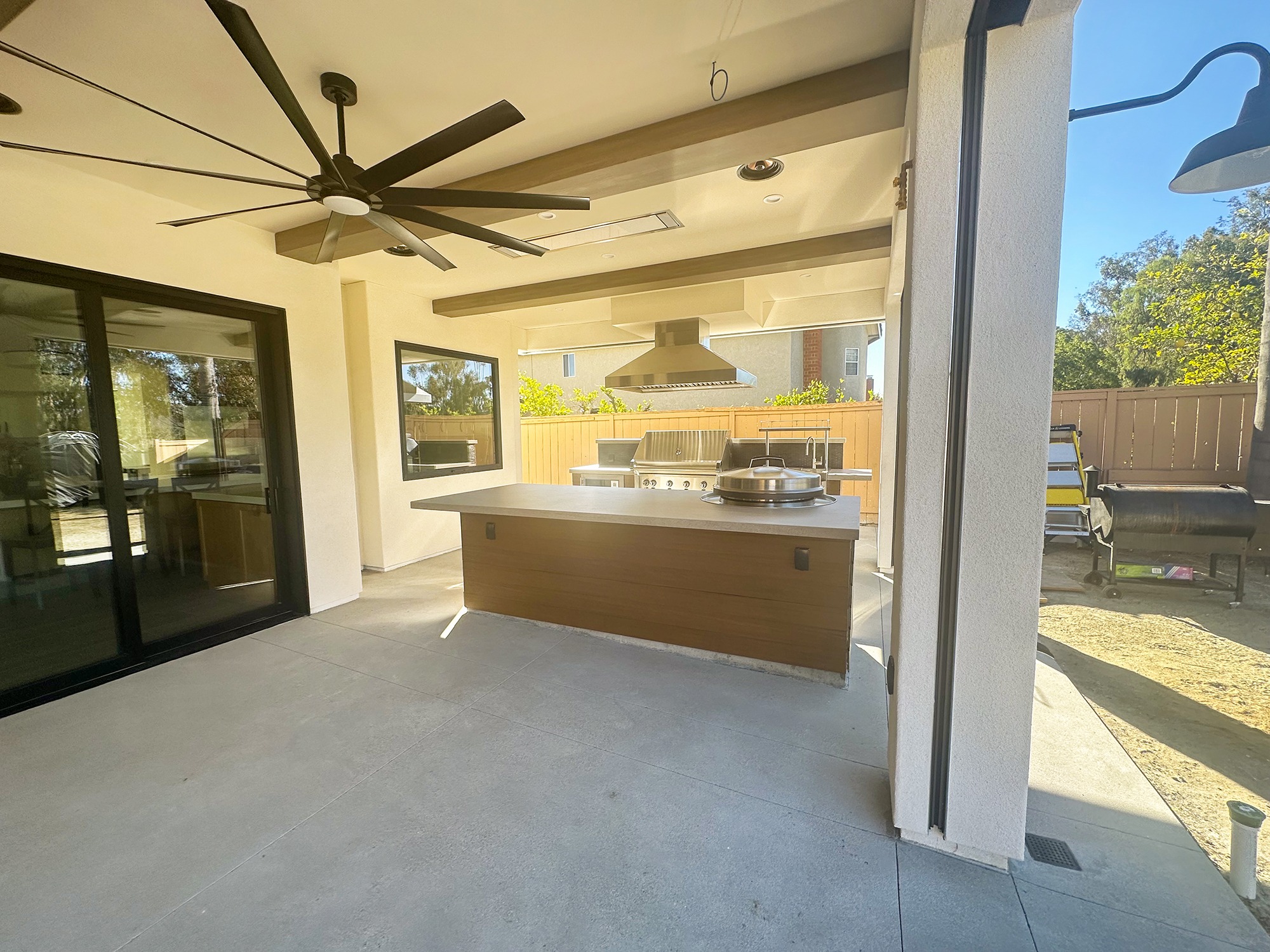 Modern outdoor kitchen featuring a large countertop, grill, and hood under a covered patio with ceiling fans and glass doors. Ideal for entertaining.